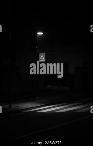 In bianco e nero girato di una strada lampada che illumina il passaggio pedonale di notte, impresso sulla carreggiata, per la sicurezza dei pedoni Foto Stock