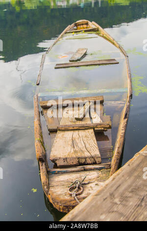 Vecchia barca in legno, canoa in un lago. Un rosso arancio imbarcazione in legno si trova sulle sponde di un lago, il riempimento con acqua Foto Stock