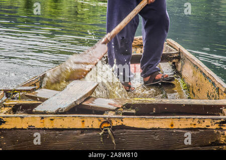 Un vecchio uomo la rimozione di acqua che ha inserito le rotte imbarcazione. Foto Stock