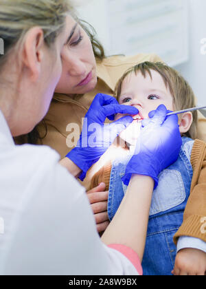 Odontoiatria per bambini. Esame dentale. Dentista considera i ragazzi i denti. Dentista femmina considera i denti. Ragazzo di età 0-1. Salute orale. Foto Stock