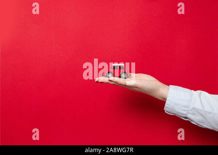 Buon Natale e Buone Feste biglietto di auguri o un banner per il sito web. Mano femmina con una maglietta blu contiene un rosso modello di auto su un rosso scuro dello sfondo con copia Foto Stock