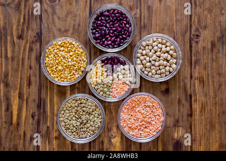 Diversi legumi in ciotole. Lenticchie, ceci, fagioli, ceci su uno sfondo di legno Foto Stock