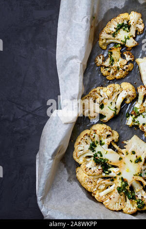 Il cavolfiore bistecche con il coriandolo lime salsa chimichurri.Vista dall'alto su un vassoio da forno e carta con spazio copia.mangiare sano Foto Stock