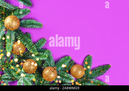 Scheda di Natale con brunch fir, palline dorate e luci su sfondo viola. Appartamento laico, vista dall'alto, copia dello spazio. Foto Stock
