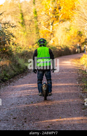 Un uomo che cavalca un monociclo elettrico lungo una ex ferrovia linea adesso un cycleway a Cannop stagni, Foresta di Dean. Autunno Foto Stock