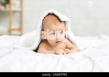 Adorable baby giacente sulla pancia ricoperta di soffice coltre bianca Foto Stock