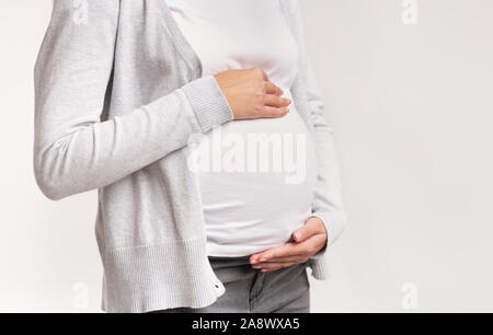 Irriconoscibile Donna Incinta toccando ventre in piedi su sfondo bianco, tagliato Foto Stock