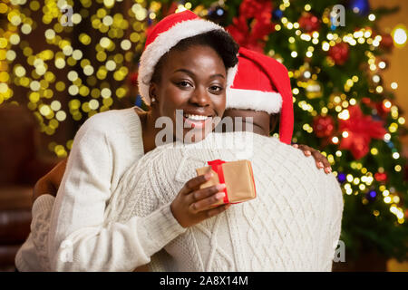 Felice donna afro abbracciando il suo fidanzato e azienda confezione regalo Foto Stock
