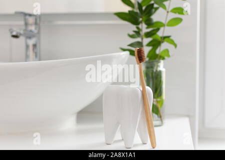 Brown bio-degradabile, compostabile bamboo spazzolini da denti a forma di dente cup in un bagno interno bianco. Pianta verde decor in background. Foto Stock