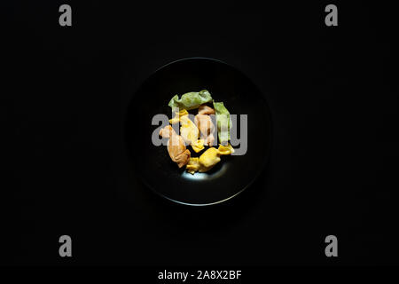 Paste alimentari farcite con forma di caramelle servito in una tazza di colore nero su uno sfondo nero in vista superiore in studio Foto Stock