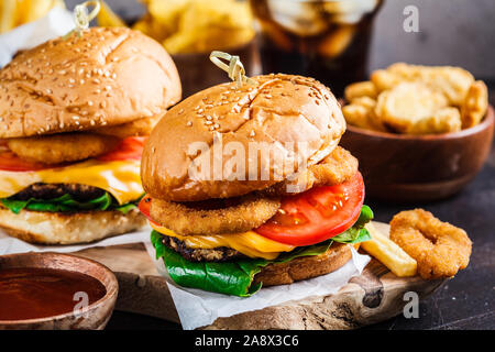 Assortimento di fast food. Il cibo spazzatura sfondo. Cheeseburger, patatine fritte, nachos, ciambelle, soda e pepite su sfondo grigio. Foto Stock