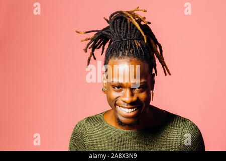 Ritratto di un felice, sorridente giovane con cool dreadlocks acconciatura guardando la telecamera, isolato in rosa Foto Stock