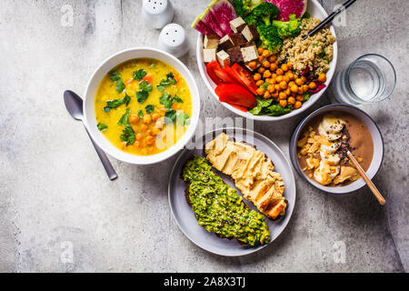 Piatto vegano laici cibo. Frullato al cioccolato ciotola, Buddha ciotola con tofu, ceci e la quinoa, zuppa di lenticchie e toast su sfondo grigio. Foto Stock