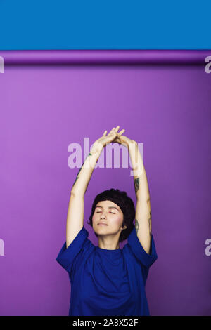 Vista ritagliata della bella donna stretching con mani overhead su sfondo viola. Foto Stock