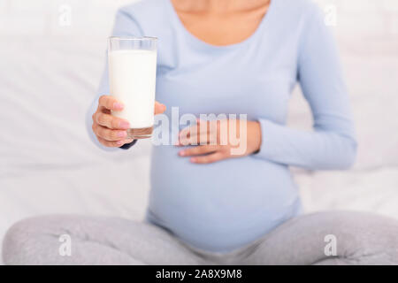 Irriconoscibile la donna incinta che offre un bicchiere di latte seduta sul letto Foto Stock