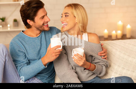 Paio di ridere a bere caffè e parlare seduto sul divano Indoor Foto Stock