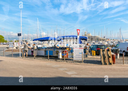 I pescatori locali in una cabina di verniciatura alimentare vendere pesce fresco con un porto pieno di yacht e barche nel porto di Antibes, Francia, sulla Riviera francese Foto Stock