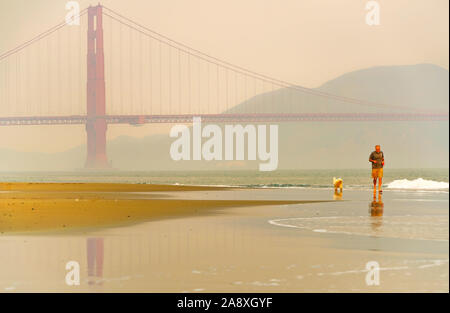 Vista del Golden Gate Bridge con gente e il suo cane che fa jogging lungo la East Beach a San Francisco all'alba. Foto Stock