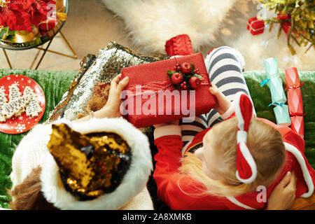 Vista superiore della madre dando un regalo di Natale per la figlia mentre è seduto sul divano del soggiorno moderno a Natale. Foto Stock