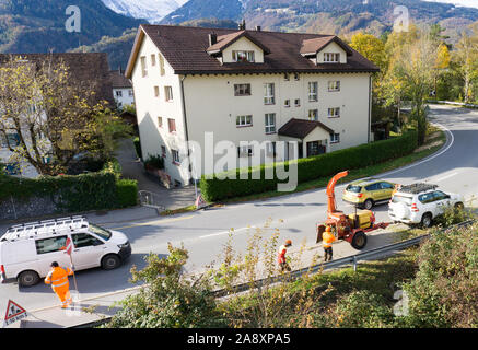 Maienfeld, GR / Svizzera - 11 Novembre 2019: città equipaggio di manutenzione con una cippatrice e shredder chiara e pulita spallamento stradale della vegetazione Foto Stock