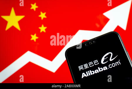 Alibaba logo sullo smartphone e uno sfondo sfocato con bandiera della Cina e una freccia che mostra la crescita. Foto concettuale. Foto Stock