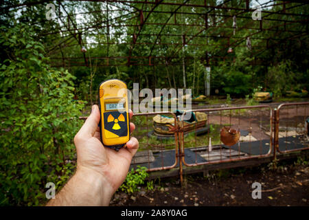 Un dosimetro in mani con un livello di radioattività in un parco giochi abbandonato nel centro di pripjat, in Chernobyl zona di esclusione, Ucraina Foto Stock