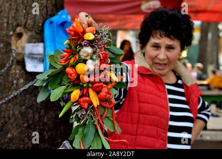 Donna in stallo del mercato mantenendo la stringa decorativo di peperoncini, aglio ed erbe aromatiche per la vendita, Foto Stock