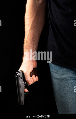 Un uomo con una pistola in mano su uno sfondo nero. Killer con una pistola Foto Stock
