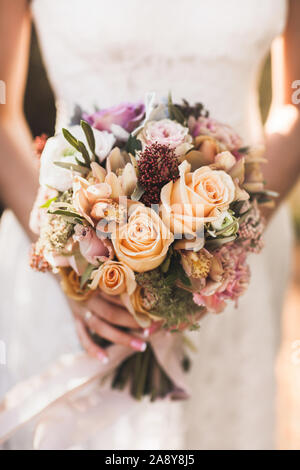Sposa tenendo nelle mani di piccoli Bouquet nozze in arancione i colori autunnali. Rosa e rose arancione, bianco peonia, fiori secchi e foglie. Foto Stock