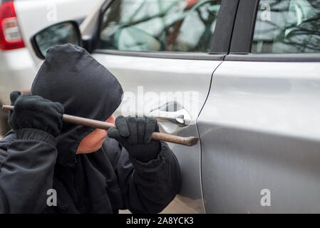 Un brigante vestita di nero che tiene palanchino a un driver in un'auto. Ladro di auto, il furto di auto concetto. Foto Stock