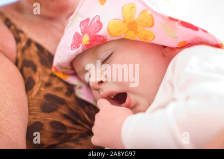 Giovani toddler sbadigli indossando un cappello floreale. Foto Stock