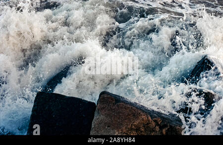 Onde che si infrangono contro un oscuro molo roccioso Foto Stock