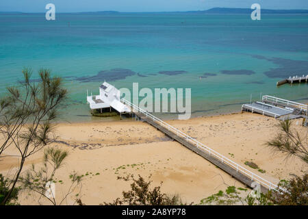 Lungo il molo di legno che si estende oltre la spiaggia nella poco profonda baia turchese acqua bianca con tettoia in legno in corrispondenza della punta Foto Stock