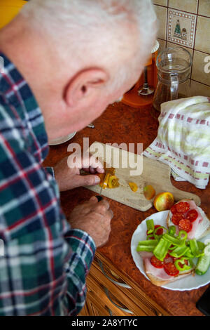 Un vecchio uomo tritare verdure su un tagliere Foto Stock