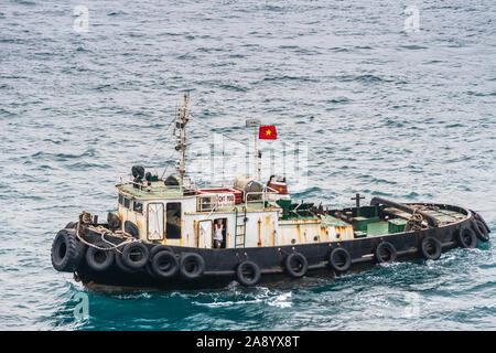 Nha Trang, Vietnam - Marzo 11, 2019: Serata, primo piano del rimorchiatore a traino con skipper visibile e bandiera nazionale sul verdognolo acqua di mare. Foto Stock