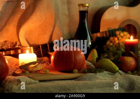 Ferma la vita raccolto di zucca, pere, mele, uva e candele luce morbida con una bottiglia di vino e la chitarra su un letto di sacco Foto Stock