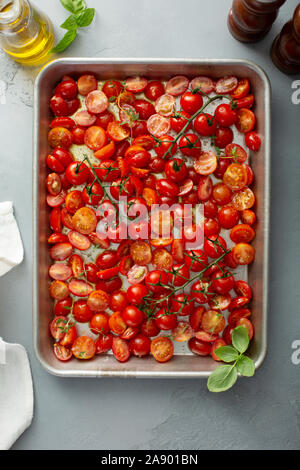 Pomodorini con aglio e spezie su un vassoio pronto per essere tostato Foto Stock