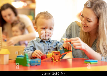 I bambini con gli insegnanti a giocare con i colori puzzle in legno in un aula montessori Foto Stock