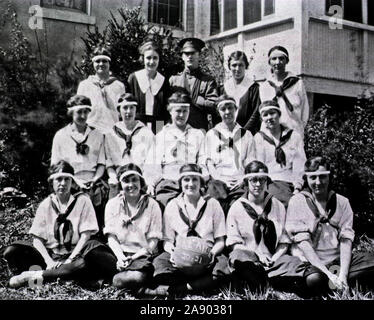 Tre righe di donne in uniformi di atletica posano per una foto di fronte ad un edificio. Nella fila posteriore, un uomo in uniforme militare si erge nel mezzo. In prima fila, la quale è appoggiata sul terreno, la donna al centro detiene una partita di basket sul quale è scritto: "Re-AIDE 20-21'. Foto Stock