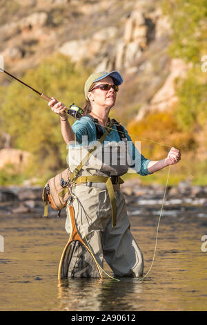 Una donna getta la sua canna da mosca e l'aspo durante la pesca in un assolato pomeriggio di caduta nel nord del Colorado. Foto Stock