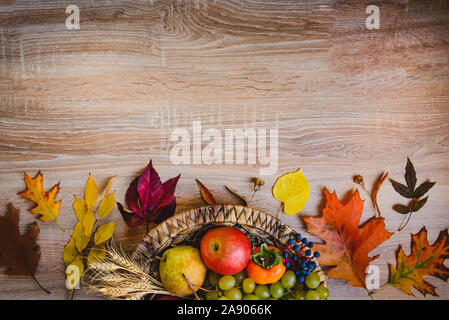 Vista superiore di vari colori d'autunno frutti e foglie in un cesto di vimini su un tavolo di legno. Copia dello spazio. Foto Stock