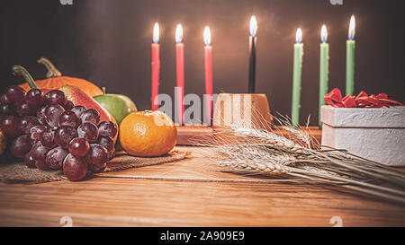 Kwanzaa holiday concetto con decorare sette candele rosso, nero e verde, confezione regalo, zucca, mais e frutta sulla scrivania in legno e lo sfondo. Foto Stock