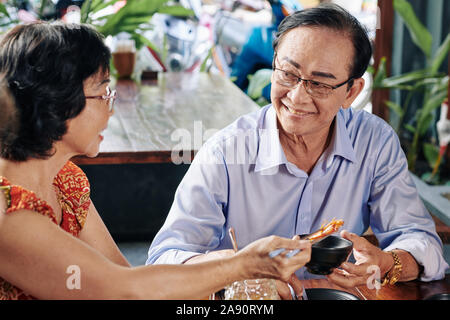 Felice vietnamita senior giovane mangiare shimps con salsa di soia durante la cena romantica nel ristorante Foto Stock
