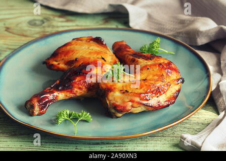 Grigliata di cosce di pollo con croccante dorato marrone pelle, prezzemolo sulla piastra bianca sul buio di tavole di legno. Sfondo di cibo. Vista superiore Foto Stock