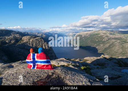 Percorso Prekestolen. Coppia con la bandiera della Norvegia guarda il panorama del Lysefjord. Attrazione turistica. Tempo soleggiato in montagna Foto Stock