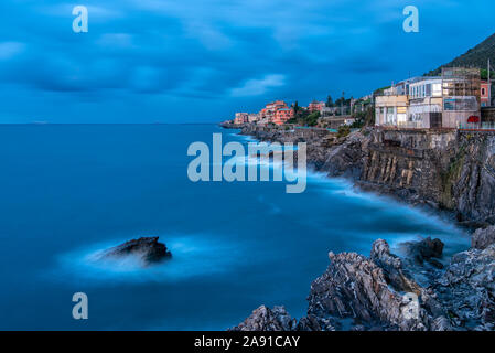 Vista lungo la costa a Nervi, Italia al crepuscolo durante ore blu con luxury waterfront ville sulle scogliere rocciose e una vista alla città in dist Foto Stock