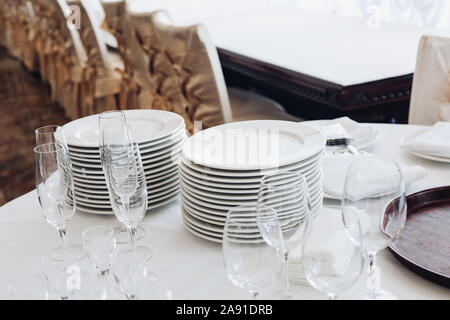 Assortimento di stoviglie sul tavolo bianco.Vista su bianco tavola rotonda con pile di piastre bianche, champagne vuota flauti e occhiali con bottiglie di Foto Stock