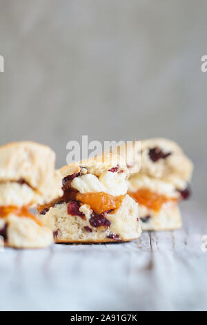 Tradizionale fresca di forno di mirtillo palustre inglese o tè ciliegia focaccine con panna e pesche burro marmellata su un sfondo rustico. Extreme backg sfocata Foto Stock