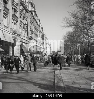 Degli anni Cinquanta, storico, Primavera e parigini nelle loro tuniche a piedi in cima alla Avenue de Champs Elysees, Paris, Francia. Foto Stock