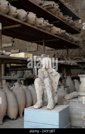 Pompei. L'Italia. Sito archeologico di Pompei. Calco in gesso di una vittima che morì in eruzione del Vesuvio nel 79 D.C., circondato da anfore fo